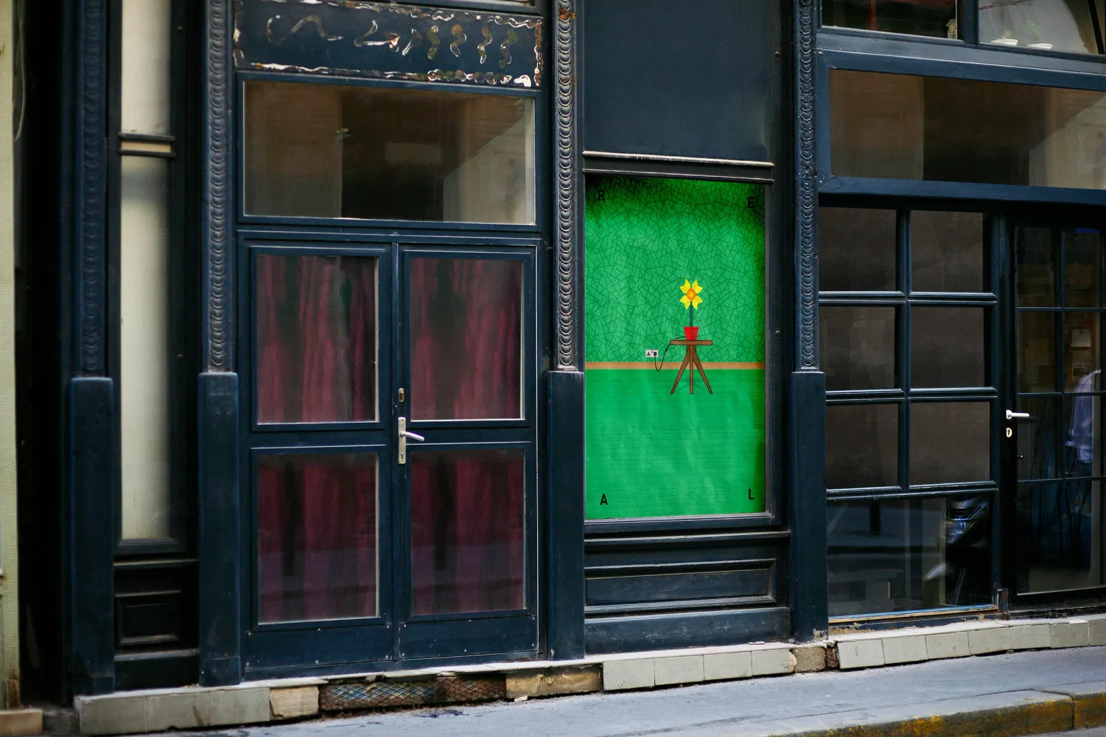 The same series in a shop window, a green panel with a cut-out letterform, seen through the glass.