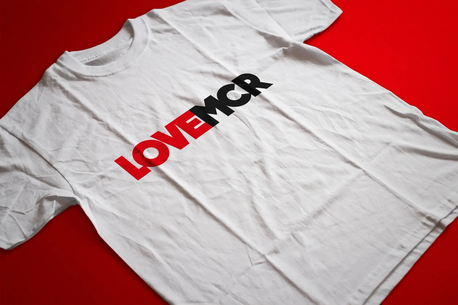 A white t-shirt on a red ground carrying the LOVE MCR wordmark across the chest.